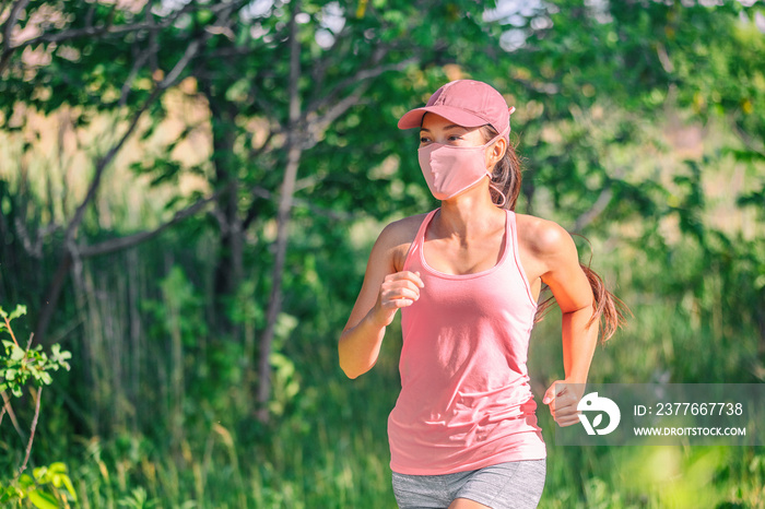 Mask wearing during exersice for COVID-19 protection Asian girl running outside with face covering while exercising jogging on run sport workout in summer park nature. Pink mask, cap, tank top.