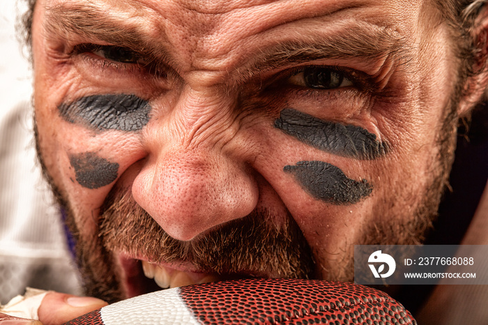 Closeup portrait of an aggressive American football player. Aggressive player bites his ball. The concept of American football, sports anger, close-up, special illumination, the effect of film grain.