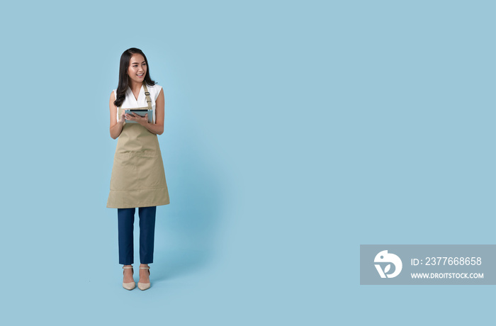 Young asian entrepreneur woman in apron hand holding tablet for list order food isolated on blue background. Barista and waitress service concept.