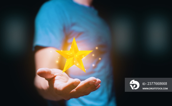 Man in a navy blue shirt holding a golden star sparkling against a black backdrop. Being a winner Concept. Being the best Concept.