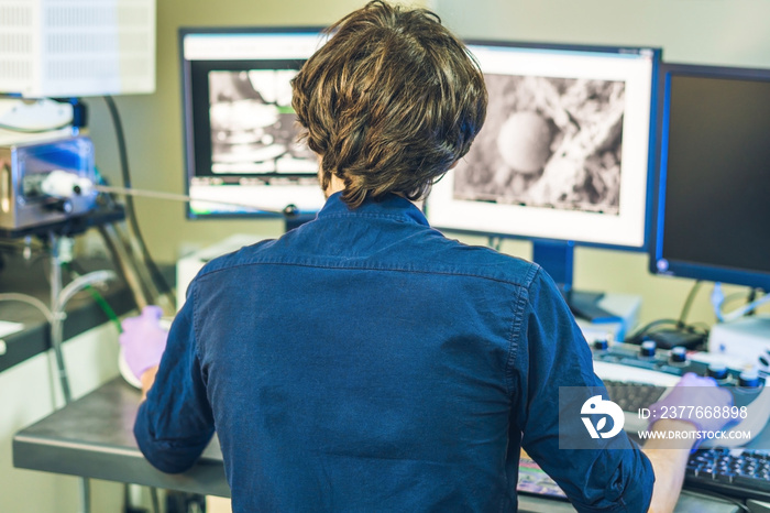 Scientist works at a electron microscope control pannel with two monitors in front of him