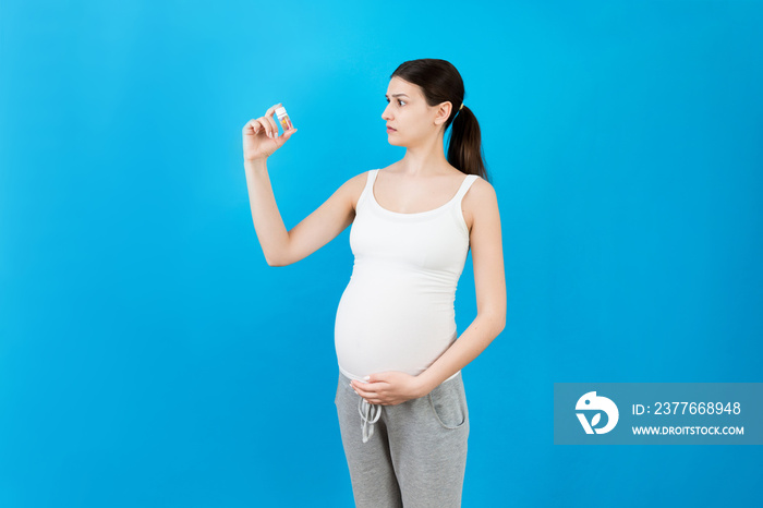 pregnant woman holding a bottle of pills against her belly at colorful background with copy space. Taking medication during pregnancy concept