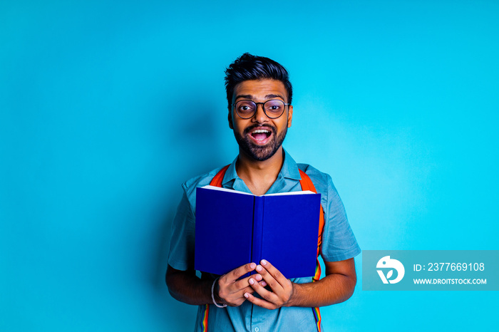 handsome young bearbed indian man with eye glasses in blue cotton t-shirt with orange rainbow backpack in studio background