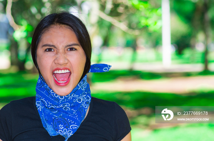 Young brunette woman wearing blue bandana around neck, interacting outdoors for camera, activist protest concept