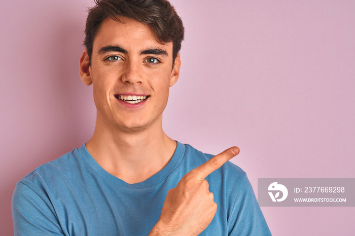 Teenager boy wearing casual t-shirt standing over blue isolated background very happy pointing with hand and finger to the side