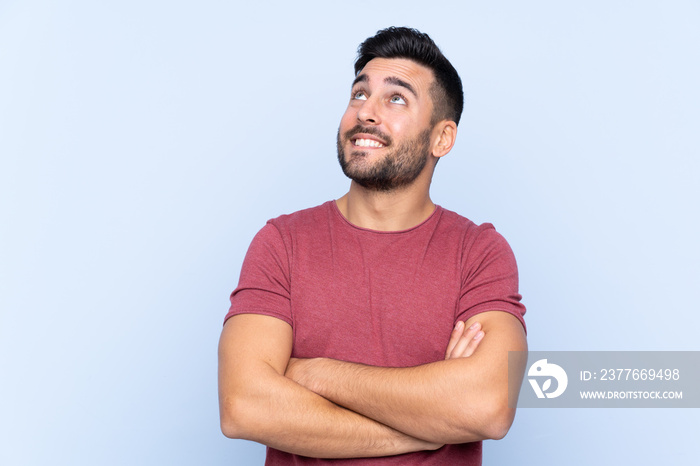 Young handsome man with beard over isolated blue background looking up while smiling