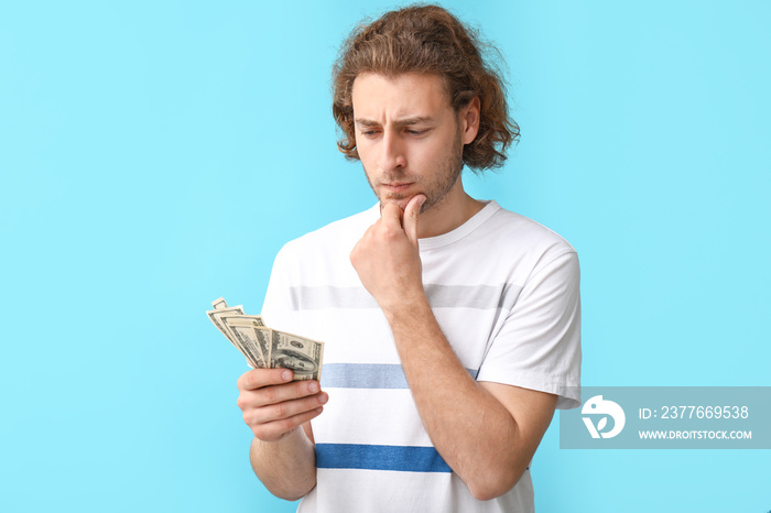 Thoughtful young man with dollar banknotes on color background