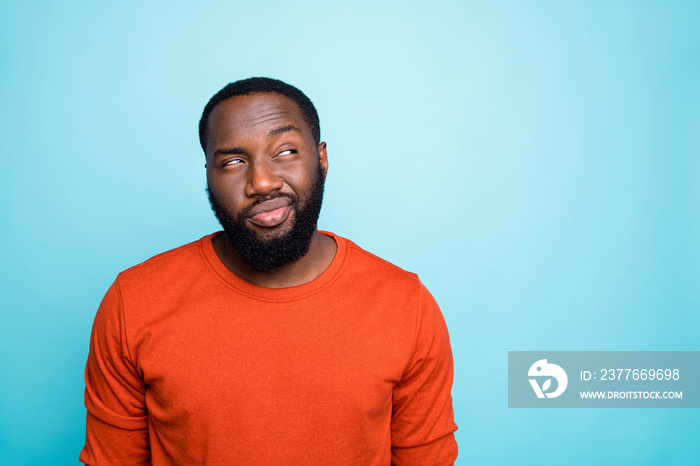 Photo of attractive dark skin guy looking tricky to empty space playful mood think over funny trick wear casual orange sweater isolated blue color background