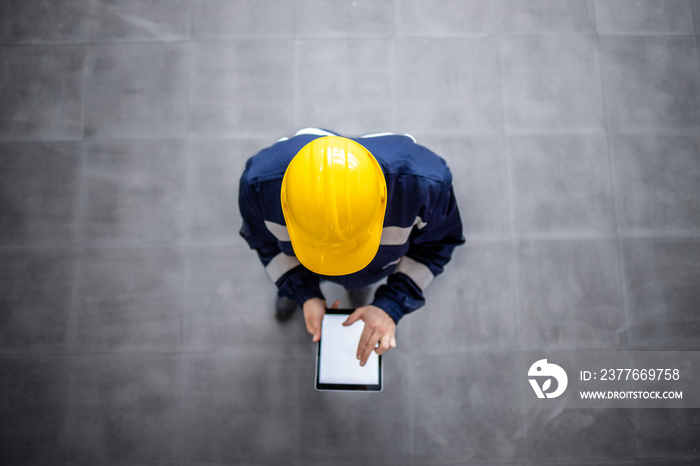 Top view of blue collar worker in work wear using digital tablet at work.