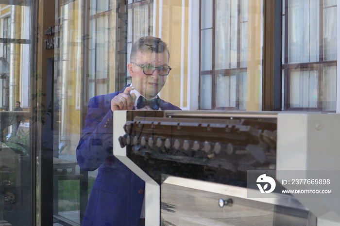 man in a blue suit looks at the printing press behind the glass