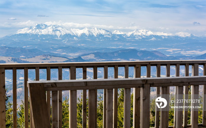 View of the Tatra mountain range from behind a wooden balustrade on an observation tower built on the Radziejowa peak in Beskid Sadecki. This peak is on the list of the Crown of Polish Mountains.