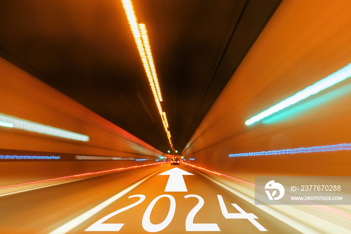 2024 text and arrow forward written on the asphalt road in tunnel with blurred light. Travel holiday concept.