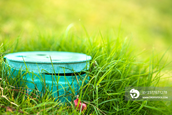 Closeup of green plastic pipe with cover on green grass lawn.