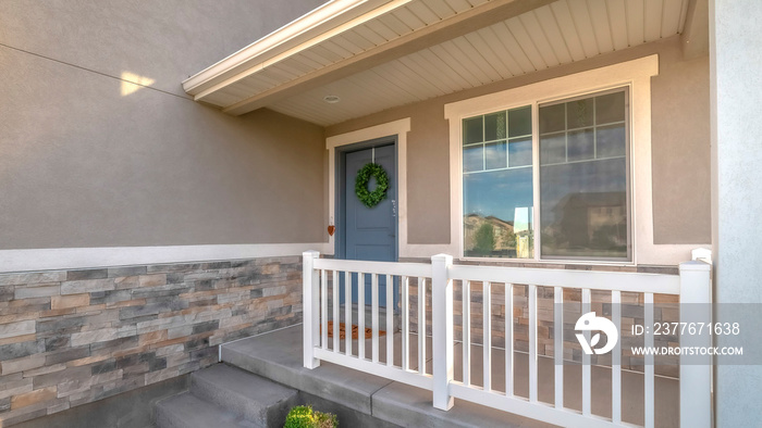 Pano Home facade with small porch and blue gray front door with green leafy wreath