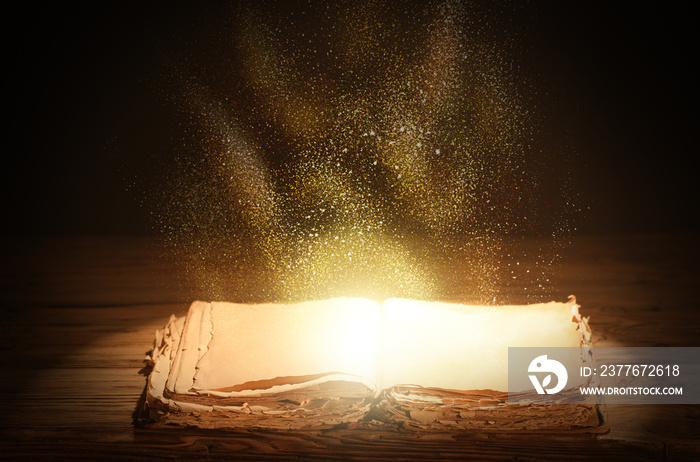 Open magic book with glow on table against dark background