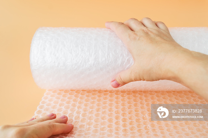 Woman hands unwind a roll of white transparent bubble wrap on a yellow background. Material for packing fragile items for safe transportation.