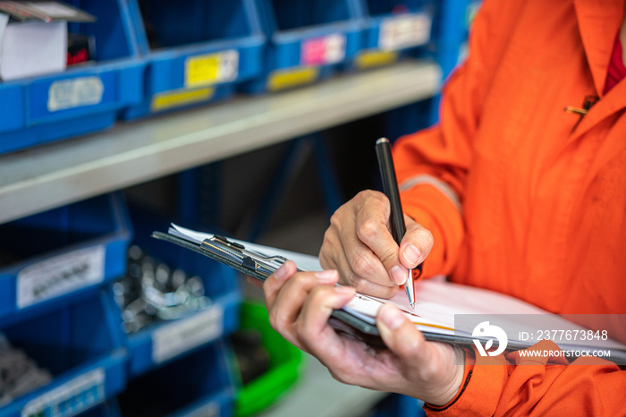 A storekeeper is performing inventory checklist with background of warehouse storage room shelf. Industrial and business working action scene, selective focus.