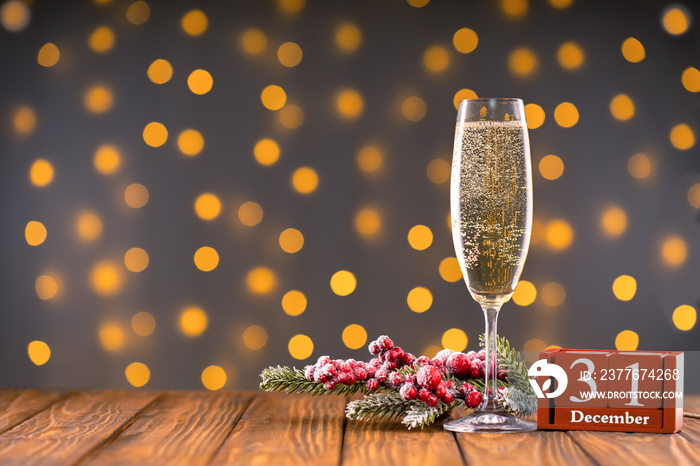 Wine glass with champagne, fir branch and perpetual calendar with date 31 december on background of blurry sparkling lights. Happy New Year holiday greeting card, banner, header with copy space