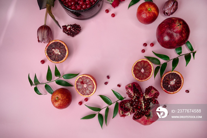 Flat lay with symbolic red fruit and berries wreath on pink background.