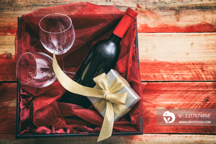 Valentines day. Red wine bottle, glasses and a gift in a box, wooden background with copyspace