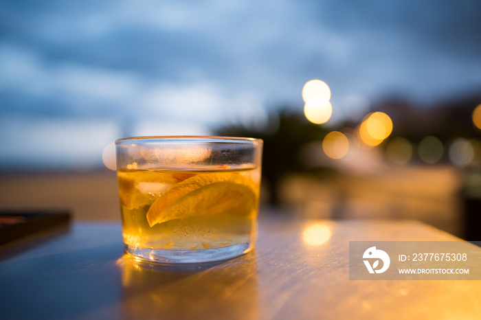 Shallow focus on the edge of fruit in a glass of delicious white sangria sitting on a bar on the beach at night. Concept of bliss happiness,and a wonderful vacation. Lovely background blur and bokeh.