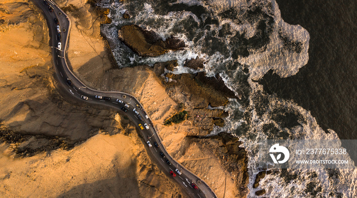 Aerial top-down view on the road at the cliffs next to the rocky coast with traffic during the sunset, Chorillos, Lima, Peru.