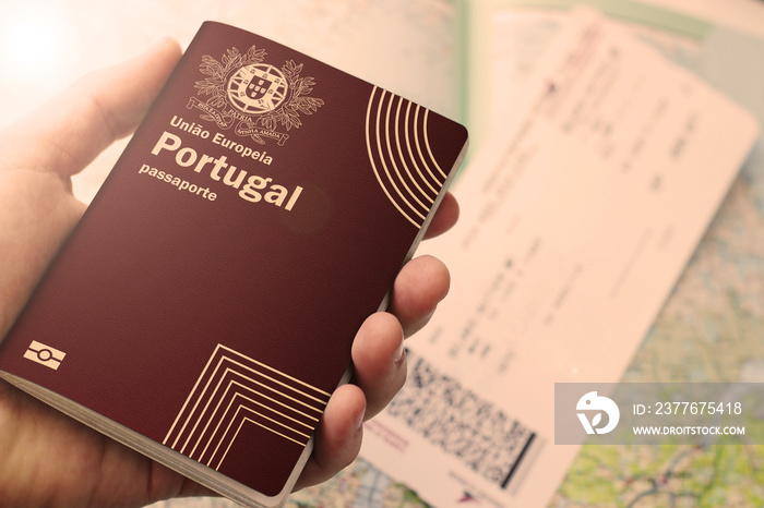 Portugal passport in a man’s hand with a plane ticket and map in the background. used to represent emigration or travelling. This image has selective focusing.