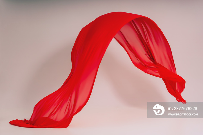 Red fabric on a white background. Levitation of red fabric in the photo studio. Soaring piece of cotton fabric. Flying colored fabric on a light background