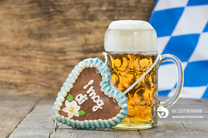 Maßkrug Bier am Oktoberfest in München mit Lebkuchenherz und bayerischer Fahne