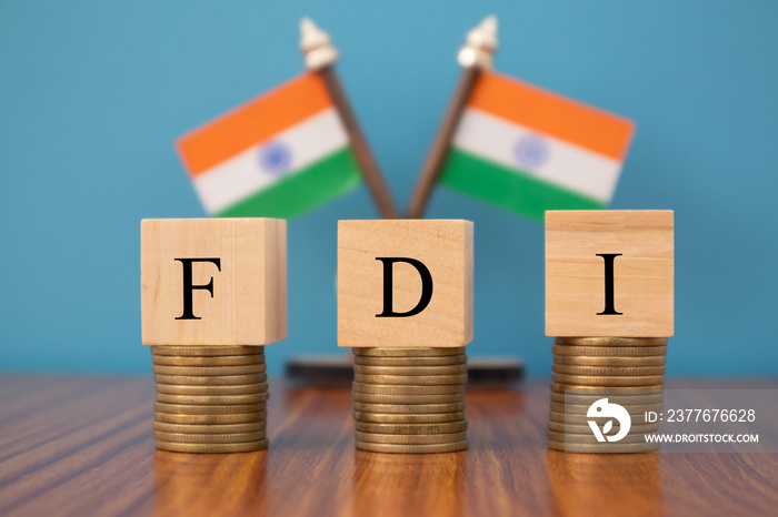 Concept of FDI or foreign Direct Investment on India in wooden block letters on stack of coins with Indian Flag as a background.