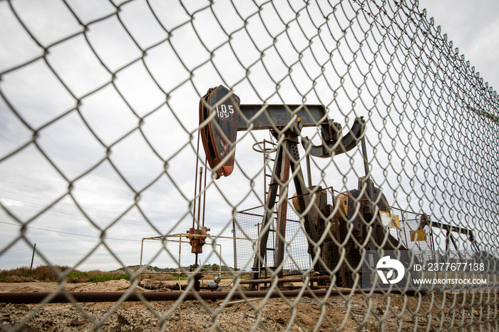 Oil Pump in Cloudy Rough Weather with Chain Link Fence