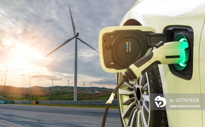 EV Car or Electric car at charging station with the power cable supply plugged in on wind mill farm. The concept of renewable energy and environmentally friendly.