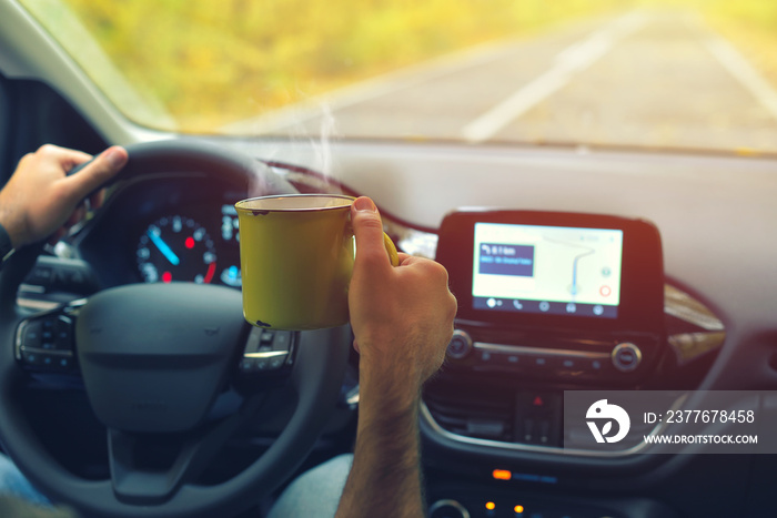 Male driver drinking hot coffee while driving on road in autumn warm colors