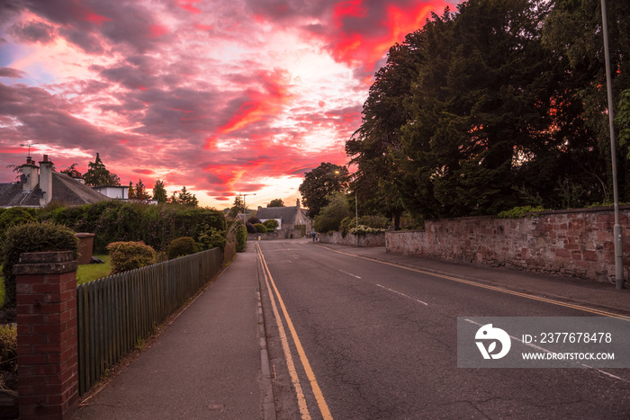 Stunning colourful sky over an empty street lined with a stone wall in a residential district at dusk