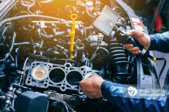 Hands of car mechanic check the vehicle engine with technical endoscope with rotary camera and mobile phone. Repair of engine head and valves.