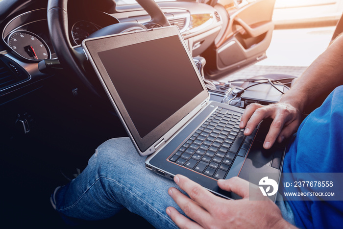 Mechanic man with laptop making car diagnostics at auto service