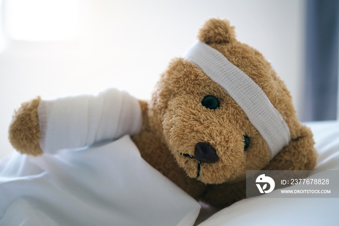 Teddy bear lying sick in bed With a headband and a cloth covered