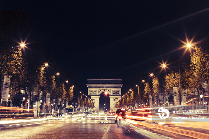 Illuminated Arc de Triomphe and the avenue Champs-Elysees in Paris. Famous touristic places and transportation concept. Night urban landscape with street traffic and city lights. Long exposure. Toned