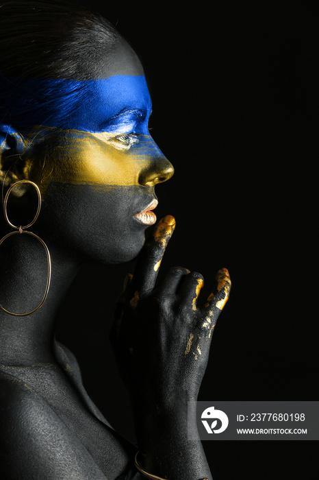 Young Ukrainian woman with blue and yellow paint on her body against dark background