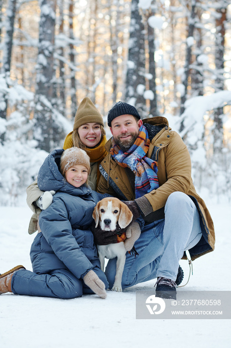 Portrait of happy family smiling at camera while walking with dog in winter forest