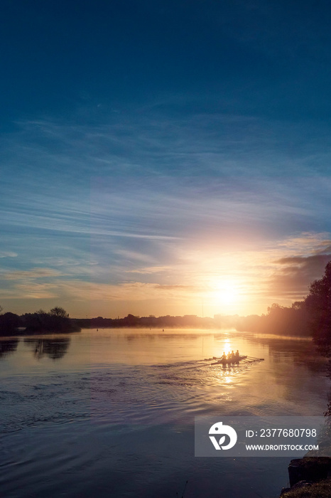 Silhouette of four athlete rowing in coxed four boat at sunrise. Rich blue and orange color. Calm and peaceful atmosphere. Corrib river, county Galway, Ireland. Stunning nature scene landscape.