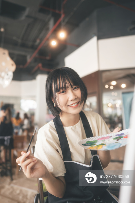 Portrait of happy young adult asian woman painting brush on canvas at workshop art lesson class.