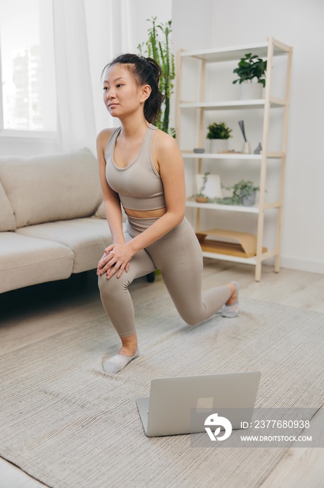 Asian woman at home exercising stretching and yoga repeating complex asanas and exercises online while looking at her laptop, home workouts on a mat to maintain a healthy body as a lifestyle
