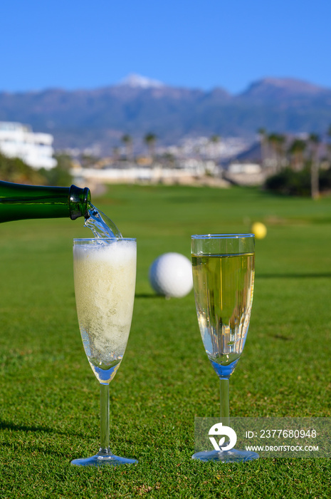 Two glasses with  bubbles white champagne or cava wine served on green golf club grass with mountains view during golf competition event or celebration