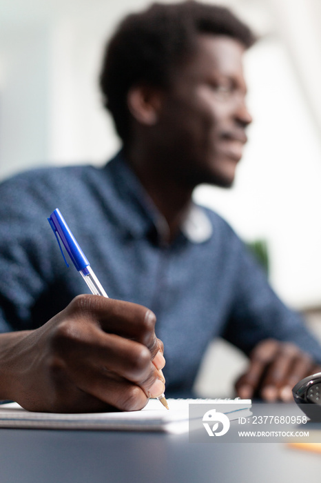 Black business student taking notes on notebook using computer, remote working from home and taking online college classes. African american man learning lessons on internet connection