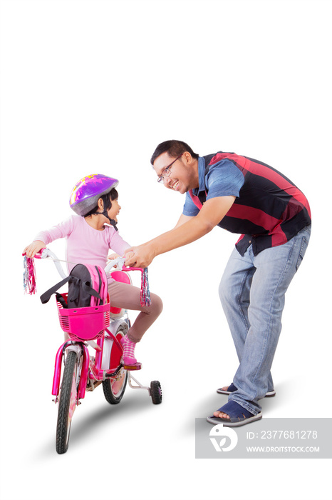 Father teaching daughter to ride bicycle on studio