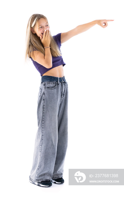 Full length portrait of cute girl in violet T-shirt and blue jeans pointing at side and smiling isolated on white background. Cute female teenager posing in studio.