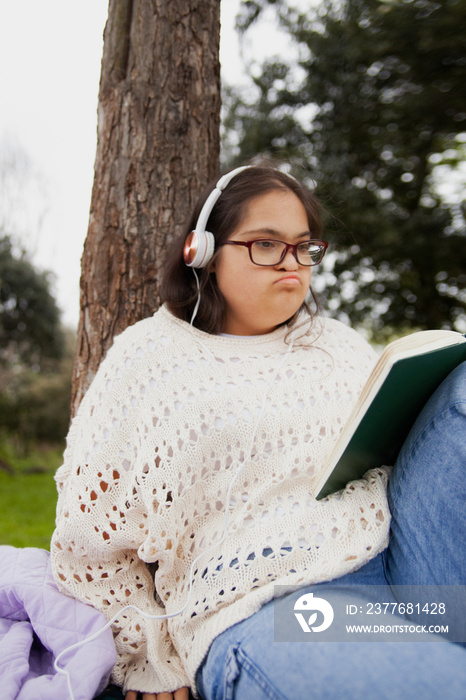 Young woman with Down syndrome reading and listening to music in the park