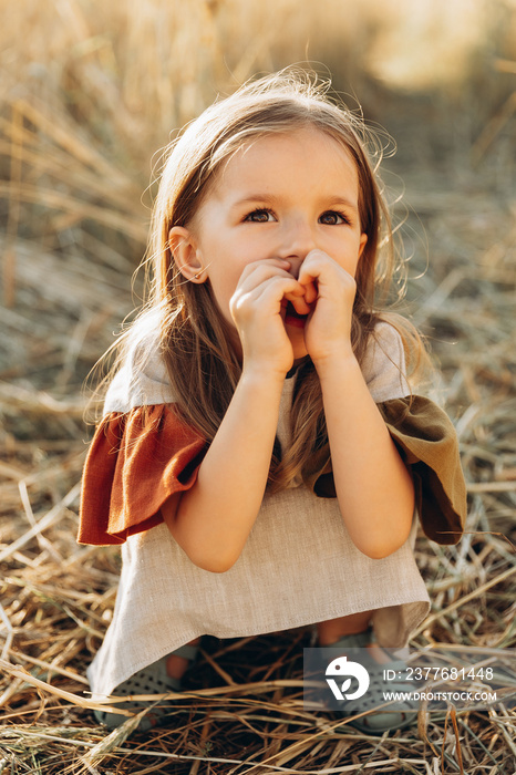 pretty 3-year-old girl walks and poses for a photo in a wheat field at sunset