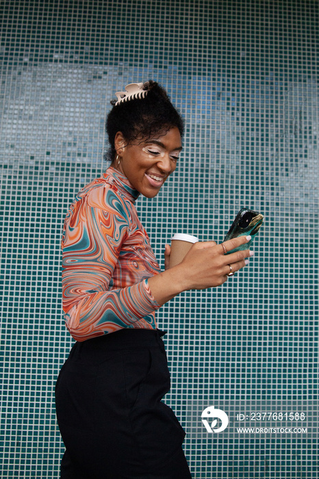 Young curvy woman with vitiligo looking at her phone in front of tiled wall